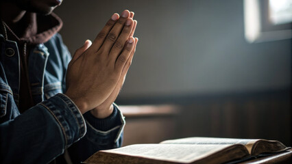 A person sits with their hands clasped in prayer in front of an open Bible. The image conveys themes of faith, spirituality, and devotion