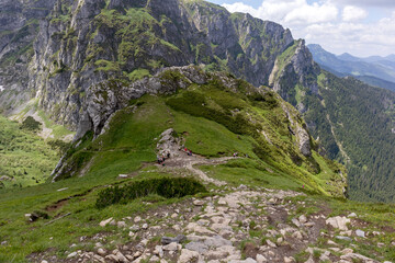 Naklejka premium A vast mountainous area with green slopes, sharp mountain peaks can be seen in the distance, the sky is covered with white clouds.