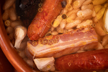 Traditional Asturian fabada cooking in clay pot with beans, chorizo, bacon, and garlic