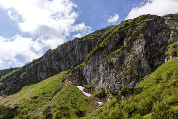 
A steep hillside with rocky walls, along which a path winds, but the lower part of the slope is covered with green vegetation.
