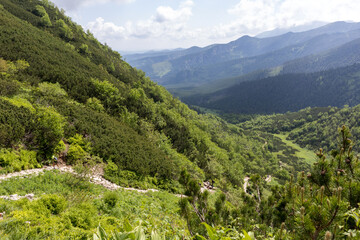 
A hilly area with green slopes with paths winding down to a valley where a small lake glistens.