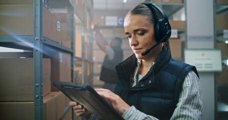 Female Logistics Coordinator Wearing Headset Uses Tablet Computer in Warehouse Facility. Sorting...