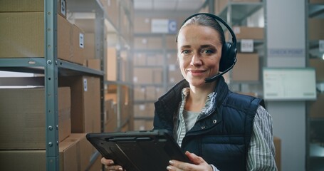 Portrait of Female Logistics Manager Wearing Headset Using Tablet Computer, Looking at Camera in...