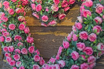 a heart-shaped wreath made of pink roses and green leaves, placed against a wooden background. The vibrant colors and heart shape make it visually appealing and suitable for romantic or decorative pur