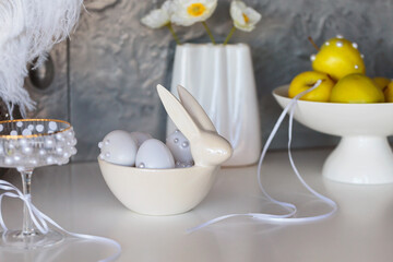 A whimsical Easter decor arrangement featuring a ceramic bowl shaped like a rabbit holding white eggs with pearl accents, alongside a bowl of yellow apples, creating a light and festive atmosphere
