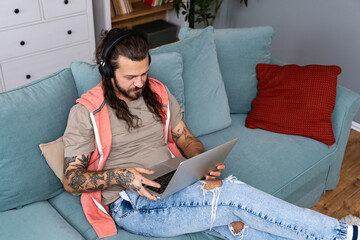Young man working from home, doing IT work from his home on laptop computer and listening to music...
