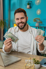 Happy rich business man counting money cash and using laptop in home office. Successful freelancer...