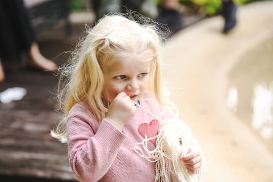 Little girl chewing on hair of doll looking thoughtful