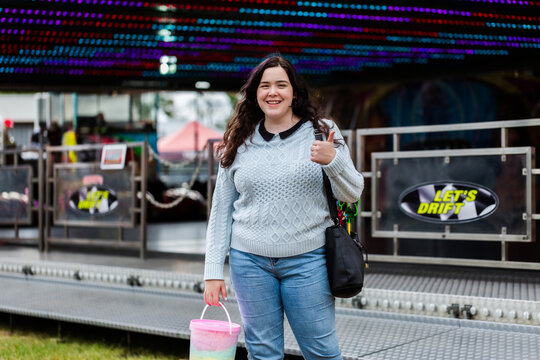 Teen young lady with bucket of coloured fairy floss by dodgem cars show ride at event