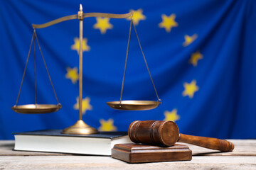 Judge's gavel, scales of justice and book on wooden table against European Union flag