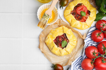 Raw galettes with tomato and basil on white tiled table, flat lay. Space for text
