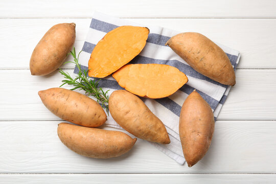 Fresh raw sweet potatoes and rosemary on white wooden table, top view