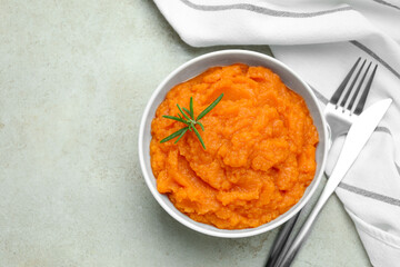 Tasty mashed sweet potato with rosemary in bowl served on grey textured table, flat lay. Space for text