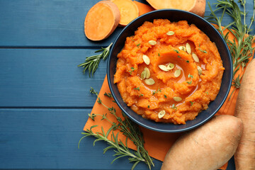 Tasty mashed sweet potato with pumpkin seeds in bowl, fresh vegetables, rosemary and thyme on blue...