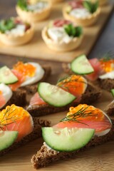 Tasty canapes with salmon and cucumber on wooden table, closeup