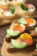 Tasty canapes with salmon and cucumber on wooden table, closeup