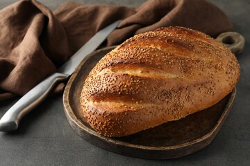 Freshly baked bread with seeds and knife on grey table, closeup