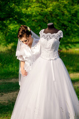 A bride is standing next to a wedding dress. The dress is white and has a lace design. The bride is smiling and seems happy