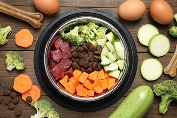 Dry and natural pet food in feeding bowl among products on wooden table, flat lay