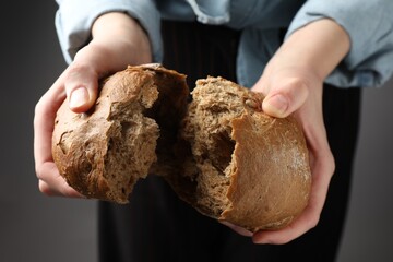 Woman breaking loaf of fresh rye bread on grey background, closeup