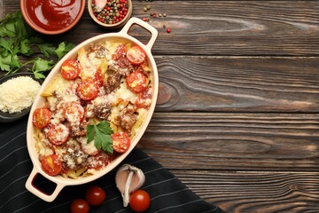 Delicious pasta casserole in baking dish with ingredients and sauce on wooden table, flat lay. Space for text