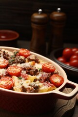 Delicious pasta casserole with cheese, tomatoes, minced meat and thyme in baking dish on table, closeup