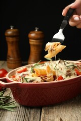 Woman eating delicious pasta casserole with fork at wooden table against black background, closeup
