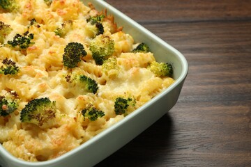Tasty pasta casserole with cheese and broccoli in baking dish on wooden table, closeup
