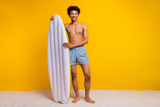 Young man with afro hairstyle stands shirtless holding a white inflatable pool float against a vibrant yellow background