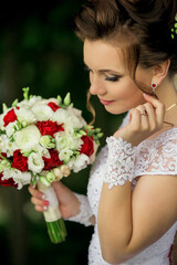 A woman is holding a bouquet of flowers and wearing a white dress. She is wearing red earrings and a ring