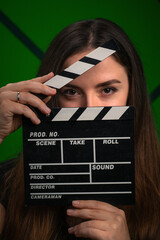 Young woman with black filmmaker clapper board on green background