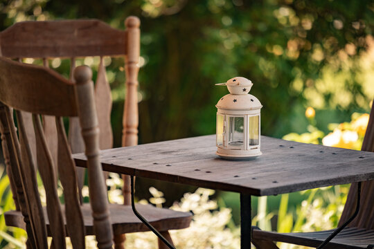Fototapeta Rustic outdoor seating with vintage lantern, wooden table, greenery, and warm sunlight