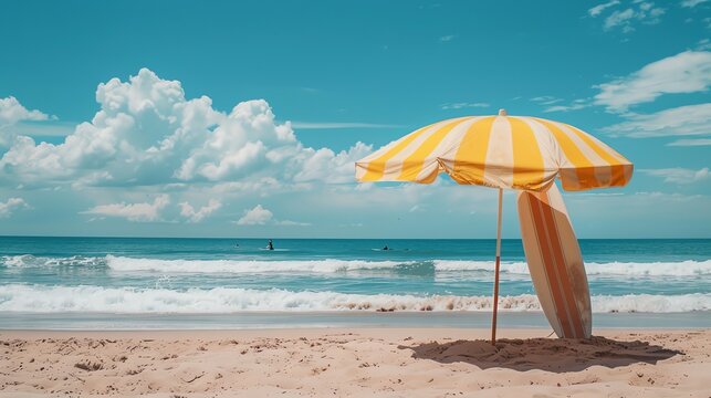 A yellow and white striped beach umbrella and a surfboard stand on a sandy beach.