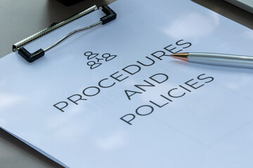 Paper clipboard displaying "Procedures and Policies" text, placed neatly on a table alongside a pen.