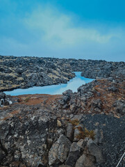 A stunning view of the Blue Lagoon in Iceland, showcasing its iconic milky blue geothermal waters surrounded by rugged volcanic rocks. The misty atmosphere 