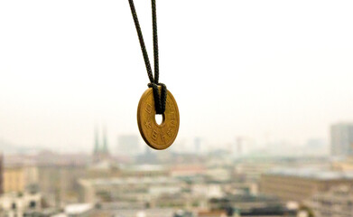 Lucky japanese 5 yen coin necklace displayed with a blurred foggy Berlin skyline in the background, symbolizing good fortune and cultural heritage. Selective focus. Copy space