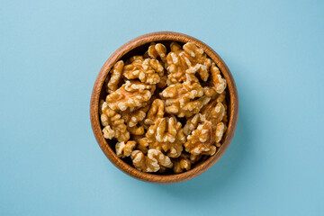 Top view of heap of walnut kernels in wooden bowl on blue background