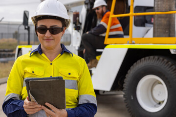 adult woman in reflective clothing holding a tablet on worksite by crane