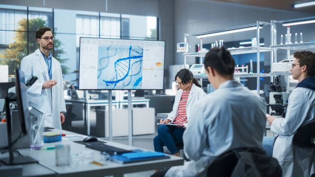 Group of Talented Female and Male STEM Students Having a Meeting with Their Teacher in a Modern Laboratory. Professor Showing a Presentation About Biochemistry or
Biophysics on Screen