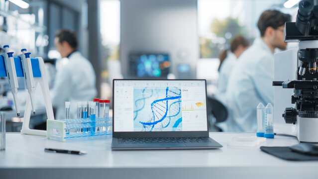 Laptop Standing on a Desk in a Modern Science Laboratory. Computer Software Analyzing DNA Sequence and Generating Report for a Research Team, Anonymous Specialists Working in the Background