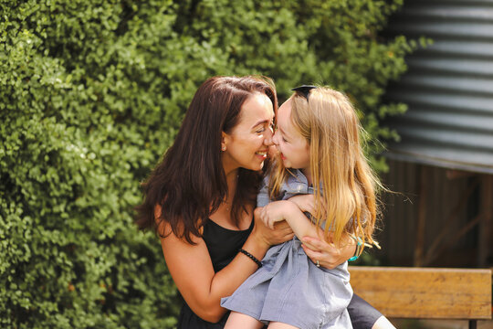 Mother and daughter snuggling in front of green hedge