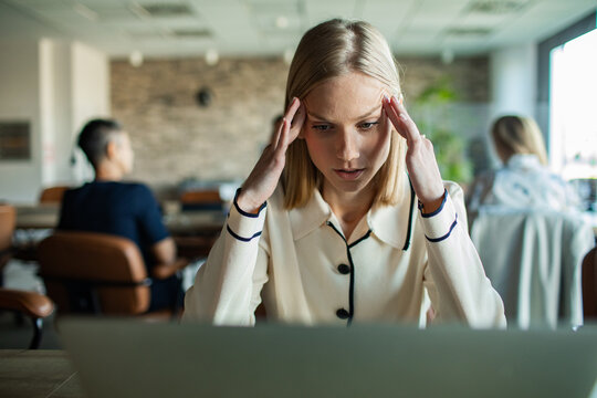Stressed businesswoman massaging temples while working on laptop