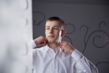 A man in a white shirt is adjusting his collar. Concept of formality and attention to detail, as the man takes care to ensure his appearance is neat and polished