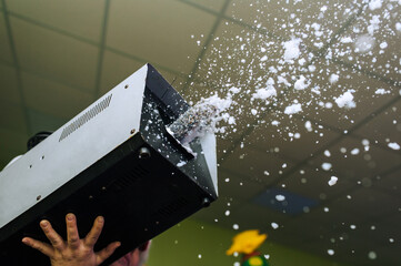 Animator holds a snow machine in his hands, from which white foam flies out, artificial snow for a...