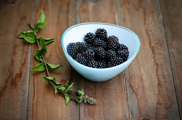 In einer Glasschale liegen viele reife Brombeeren. Daneben ein Minzezweig.
