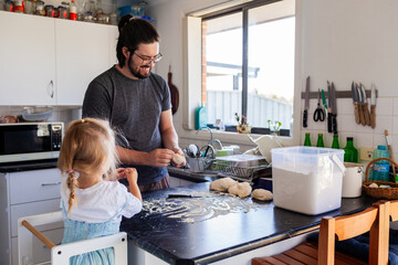 Dad with little girl in kitchen baking together making bread buns in messy home
