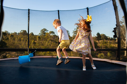 young aussie brother and sister jumping on trampoline in backyard together