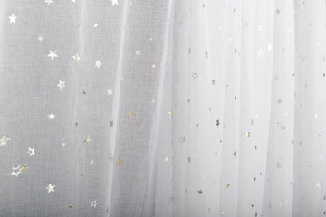 A white curtain with silver stars. The folds of this tulle.