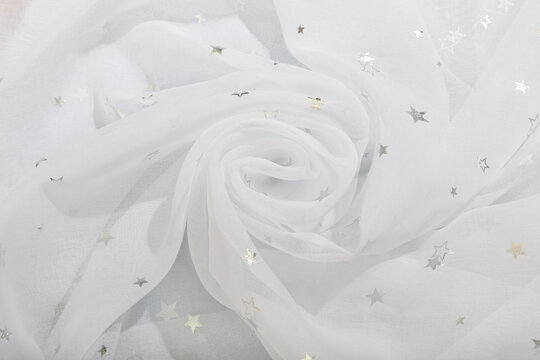 The white fabric is curled in waves into a rose. Tulle pleats with silver stars.
