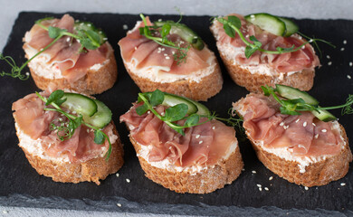 Sandwiches with soft cheese, jamon and cucumber on slate board